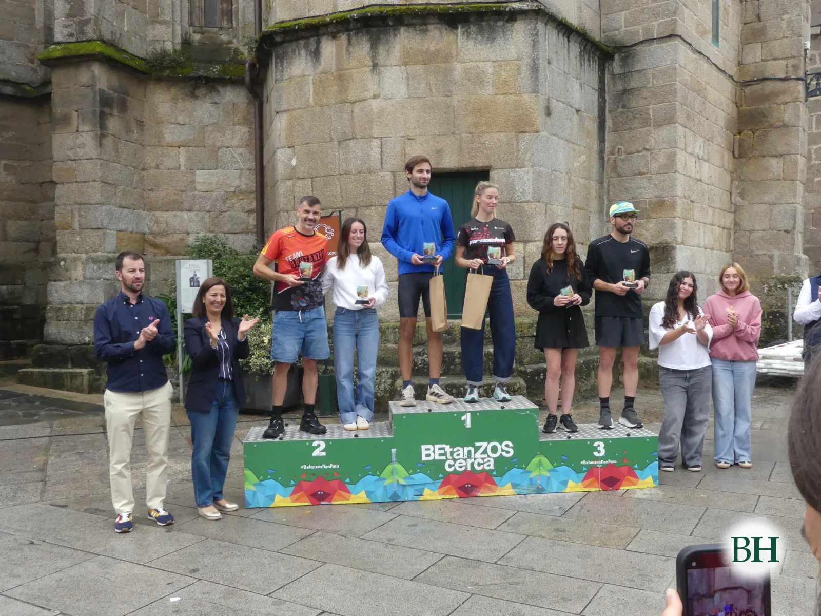 Premiados con sus trofeos en el podio, con autoridades y voluntarias alrededor, ante la Torre do Reloxo.