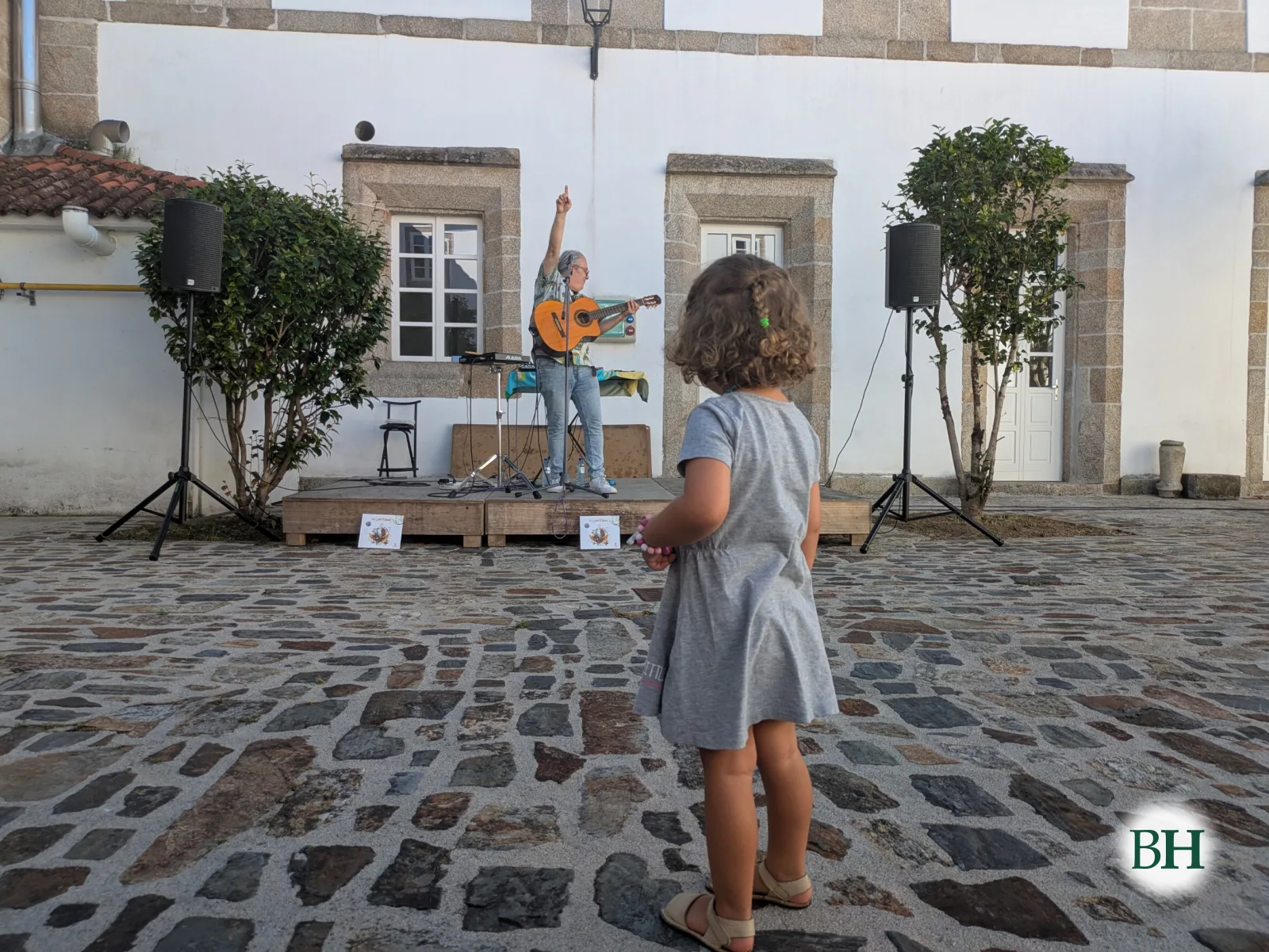 Una niña, de espaldas, mira a Chuches Amil, que toca la guitarra con el brazo en alto sobre el escenario montado en el patio del Museo das Mariñas