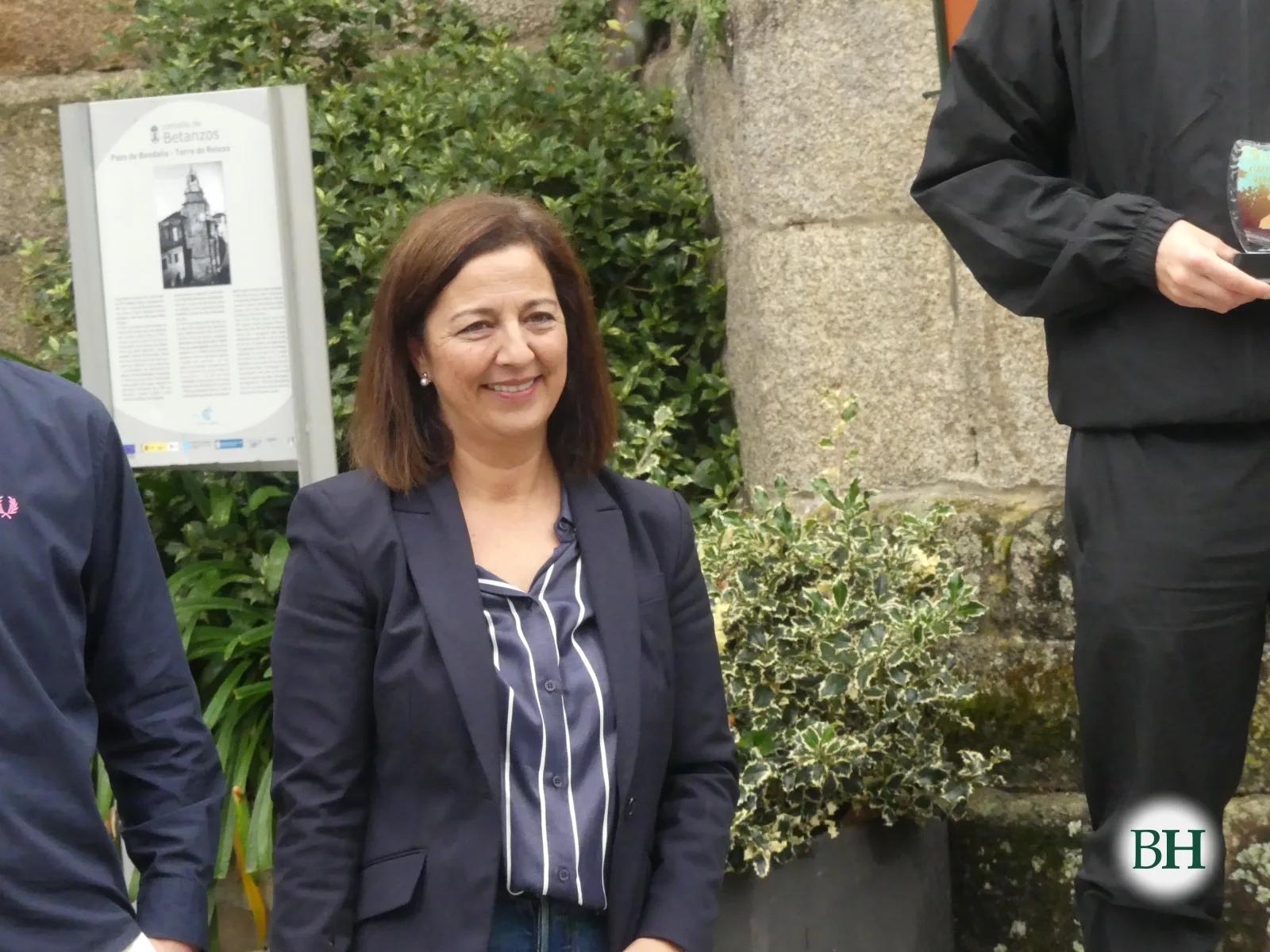 Muller con americana sorrí xunto ao cartel informativo da Torre do Reloxo durante a entrega de premios.