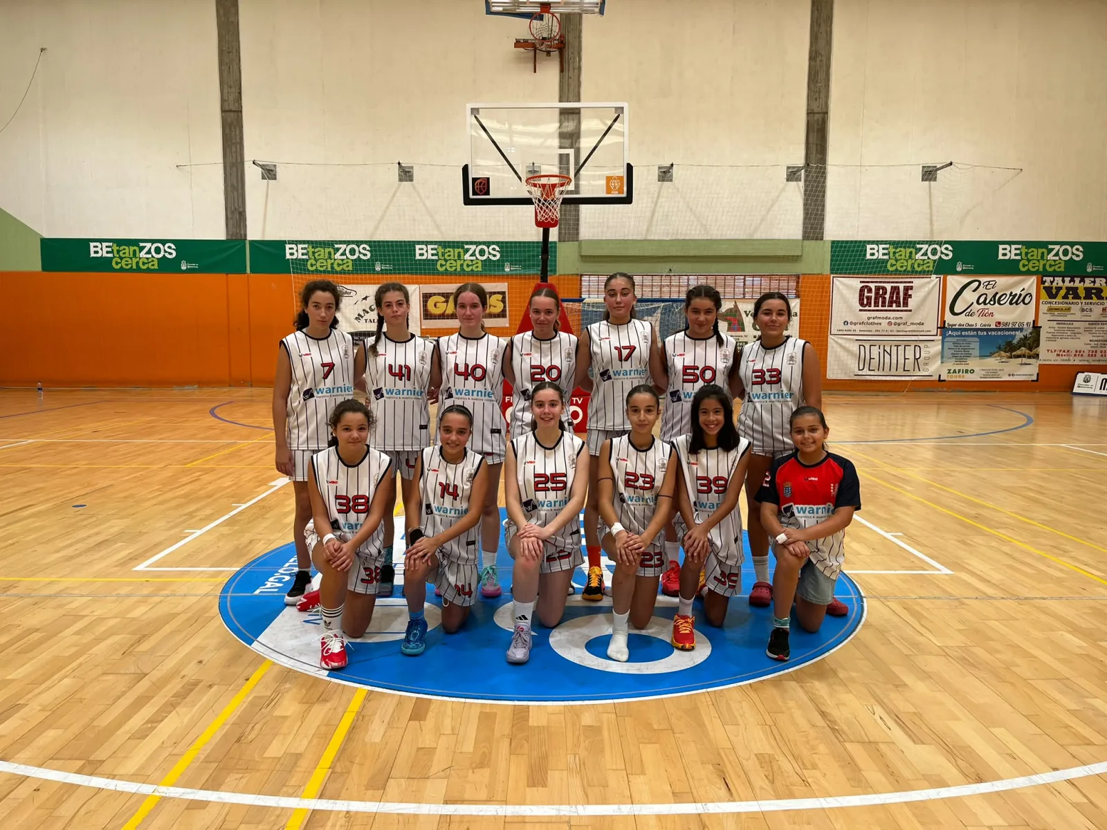 Foto de equipo del infantil femenino de Warnier Informática del Santo Domingo Betanzos, con camisetas blancas a rayas, en la pista del pabellón municipal de Betanzos.