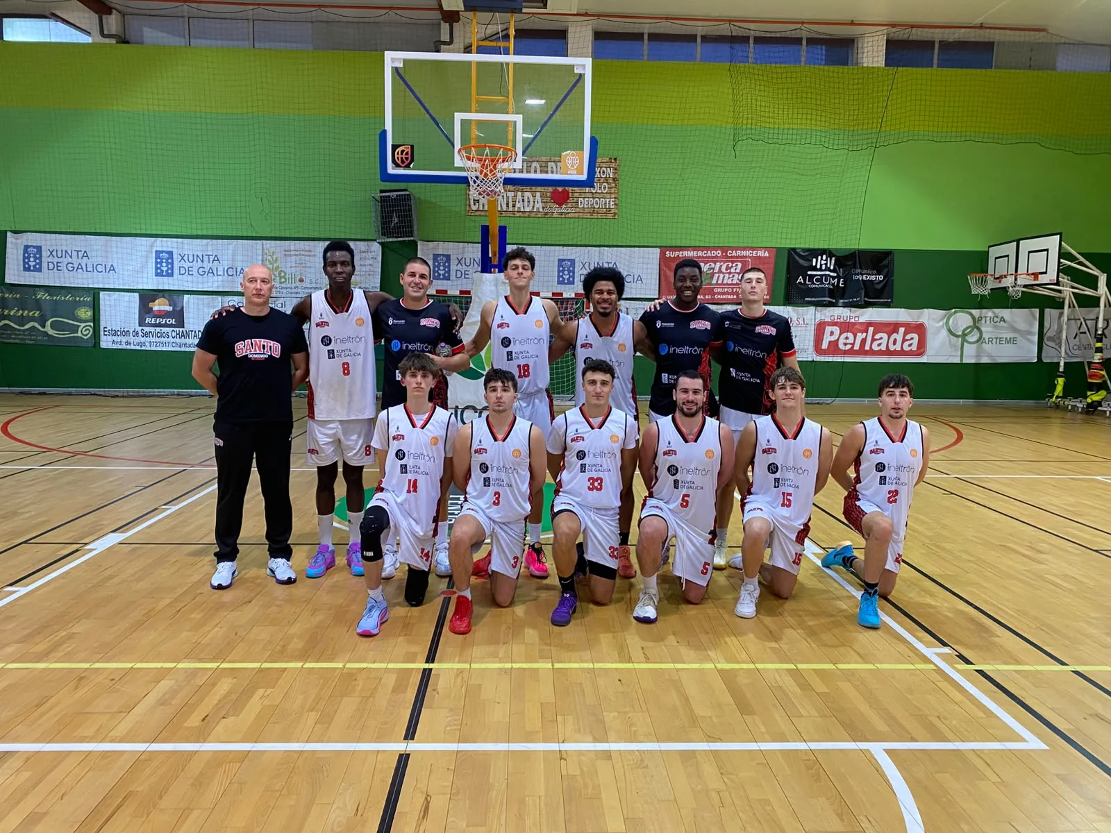 El primer equipo del Ineltrón Santo Domingo Betanzos posa en la pista del Municipal de Chantada: el cuerpo técnico y parte de los jugadores de pie, y seis jugadores arrodillados delante, con la canasta al fondo.